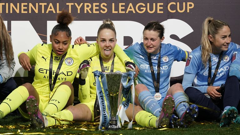 Manchester City goalkeeper Eli Roebuck poses with the trophy as her team celebrates winning the Women's Continental Tire Association Cup.